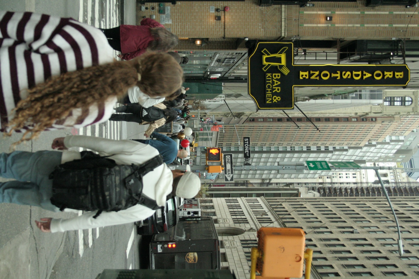 Looking up between city buildings as people walk below — motion, pressure, and space above.